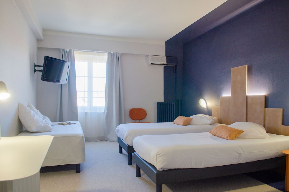 A hotel room with two beds, a TV mounted on the wall, a desk, and a chair.
