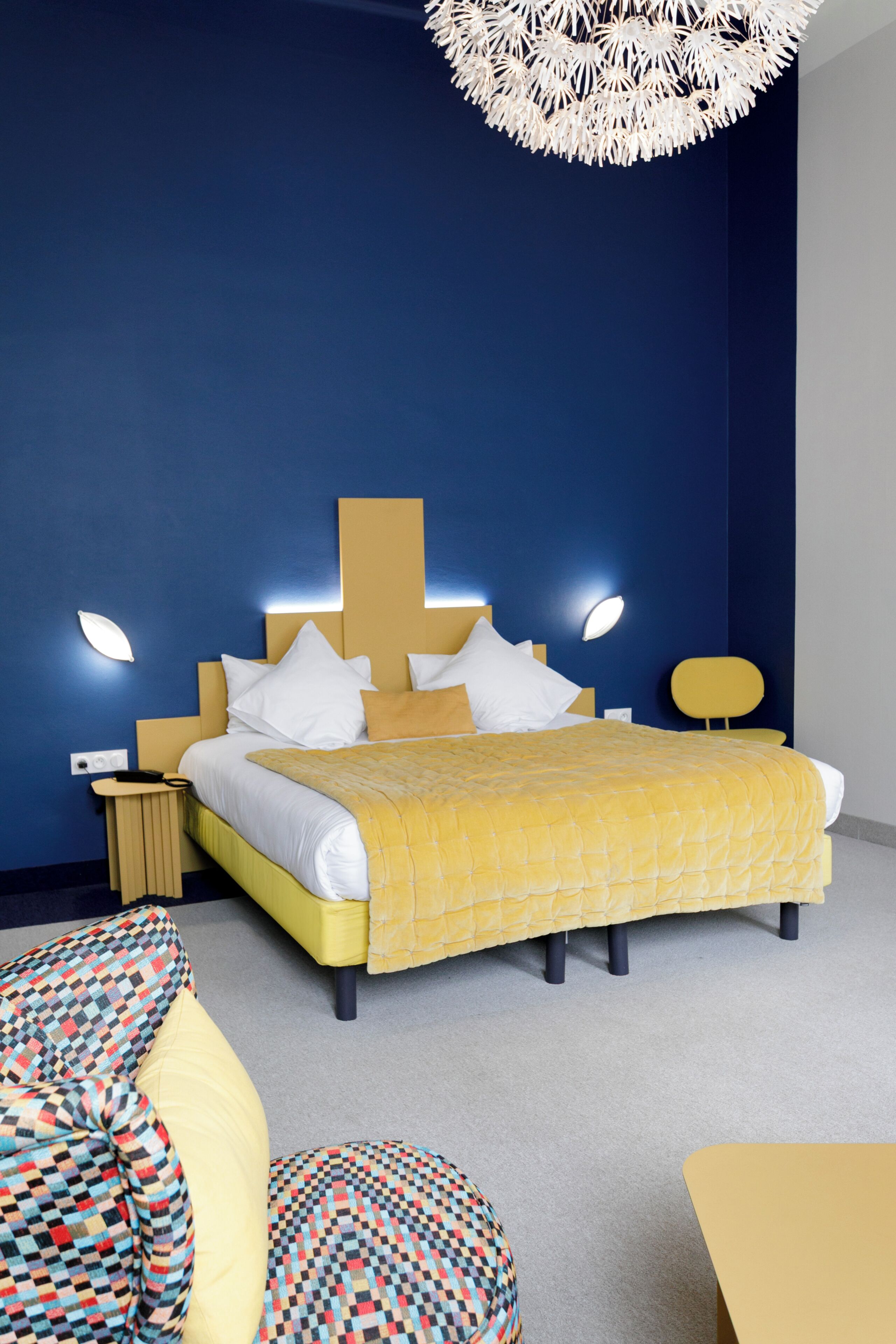 Une chambre d’hôtel moderne, dotée d’un grand lit, de tables de chevet, d’un luminaire au plafond original et d’un canapé à motifs.