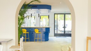 A reception area with a blue counter, two yellow bar stools, and a potted plant. - Hôtel Impérator (Béziers)