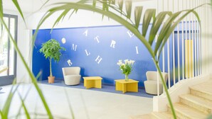 A reception area with a blue wall, white furniture, and a staircase. - Hôtel Impérator (Béziers)