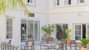 An outdoor seating area with tables and chairs, a sign for a hotel, and potted plants. - Hôtel Impérator (Béziers)