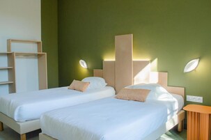 A hotel room with two beds, a wooden side table, and a green accent wall.
