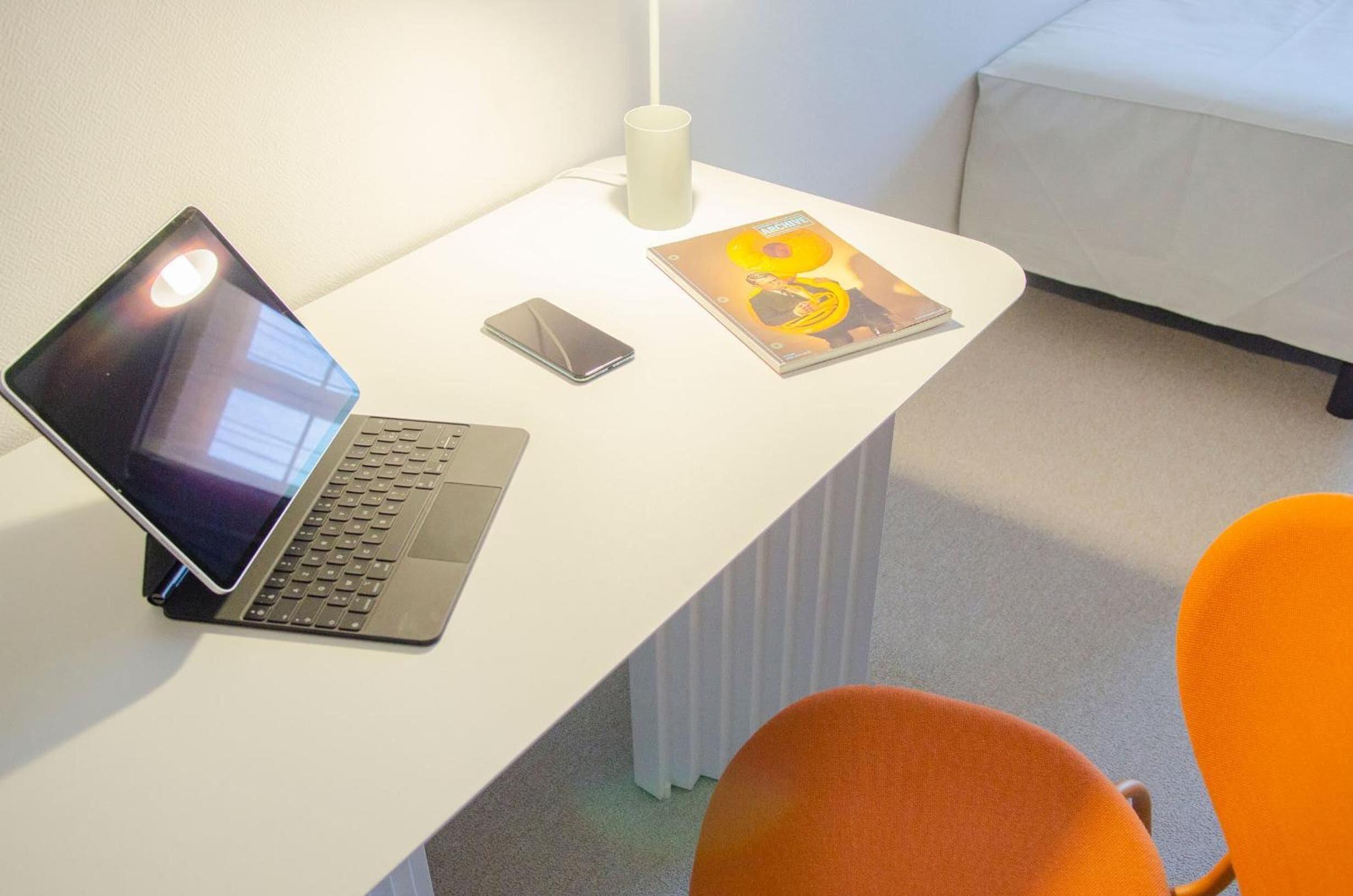 En bærbar computer, en smartphone og et magasin på et hvidt skrivebord.