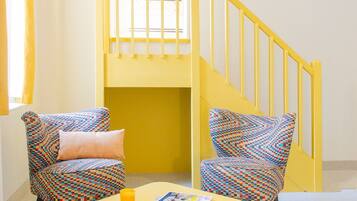 Una habitación con una escalera amarilla, dos sillas con estampado, una mesa amarilla y una ventana con cortinas amarillas.