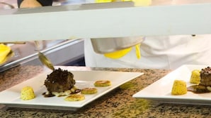 A chef in a black uniform with 'Ducal Boehlard' embroidered on it, preparing food in a kitchen. - L'Esplanade (Domme)