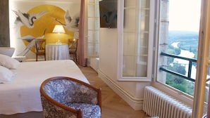 A hotel room with a bed, a chair, a table, a lamp, a painting, and a view of the outdoors. - L'Esplanade (Domme)