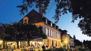 A historic building with a prominent central tower, arched windows, and a courtyard with people gathered around. - L'Esplanade (Domme)