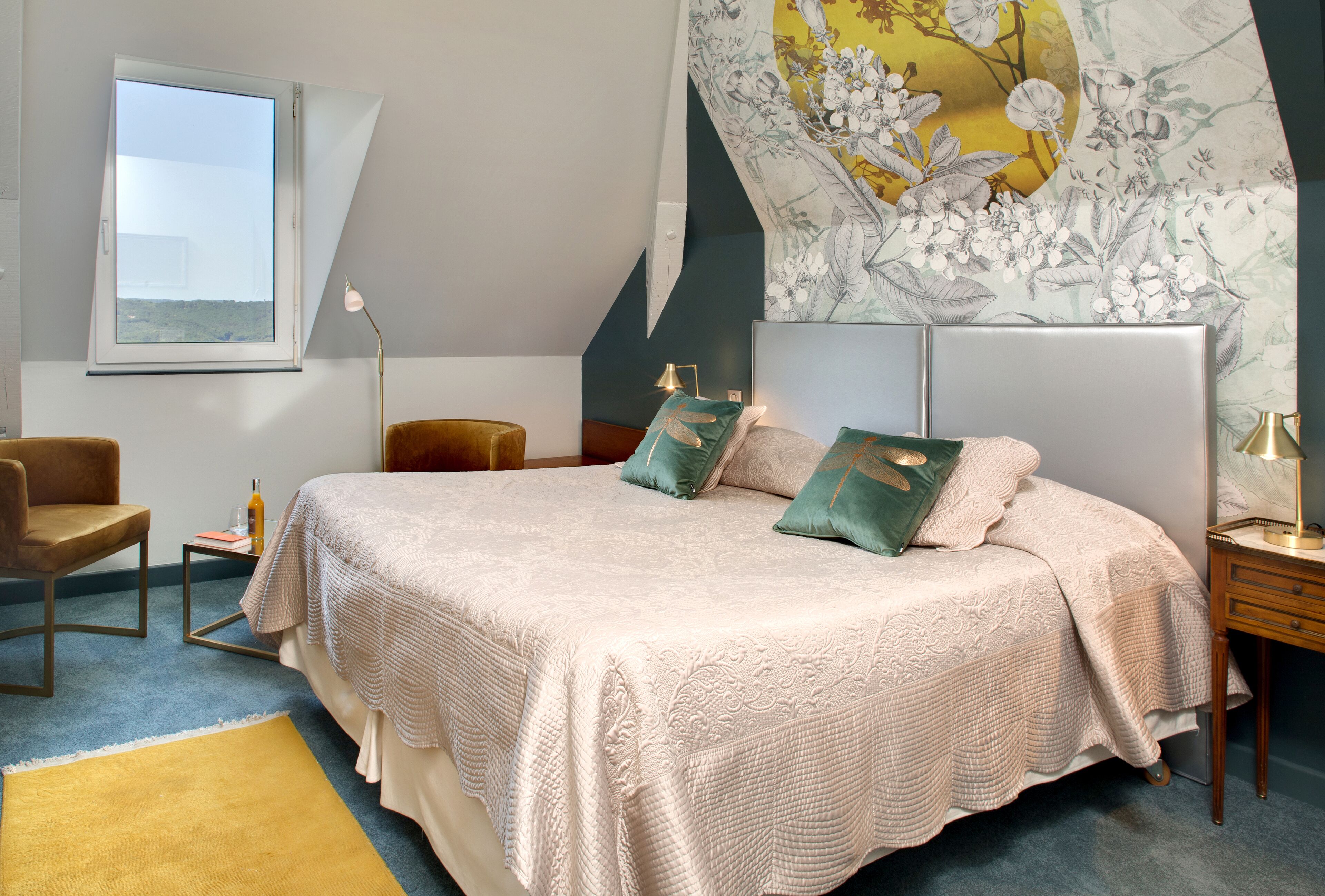 Un dormitorio con una cama grande, un escritorio, una silla, un ventanal y una pared con un mural floral.