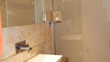 Un baño moderno con ducha de vidrio, un espejo grande y un tocador de madera con lavabo.