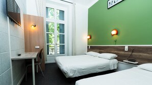 Habitación de hotel con dos camas, un escritorio y una silla. Hay luces empotradas en la pared y una ventana con cortinas.