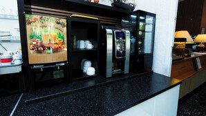 Una kitchenette con cafetera, refrigerador y una exhibición de frutas y tazas de café.