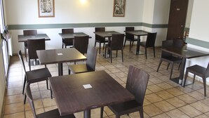 A restaurant with multiple tables and chairs, framed pictures on the walls, and a door in the background. - Citotel les Alizes (Eysines)