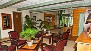 A lobby with wooden furniture, potted plants, and a reception desk. - Citotel les Alizes (Eysines)
