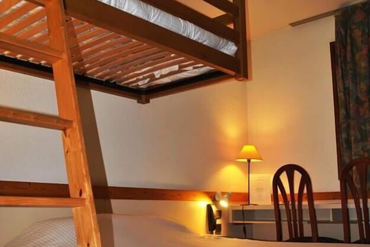 A bunk bed room with a wooden ladder, a desk with a lamp, and a chair.
