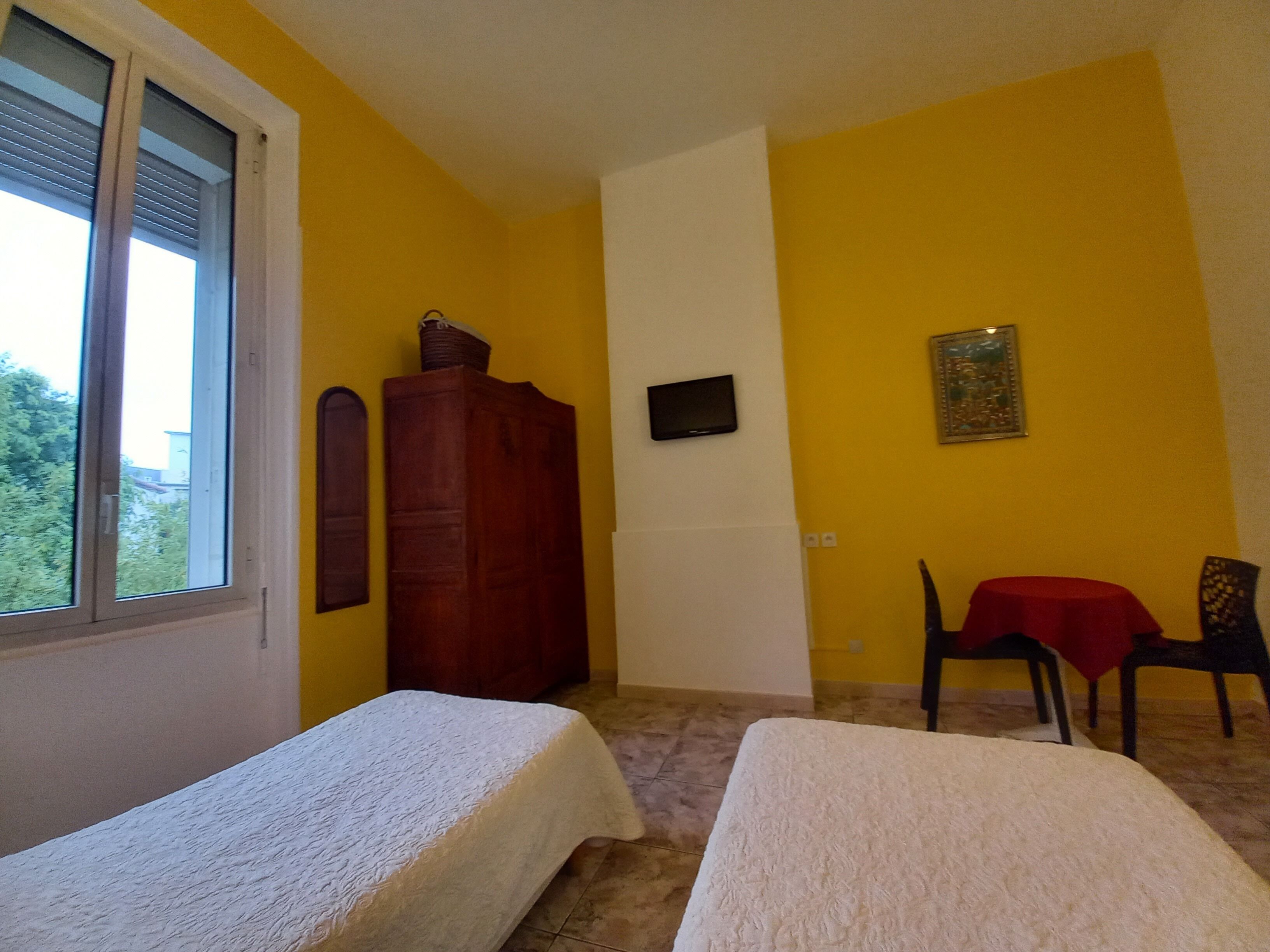 A room with two beds, a wooden wardrobe, a television, and a table with a red tablecloth.
