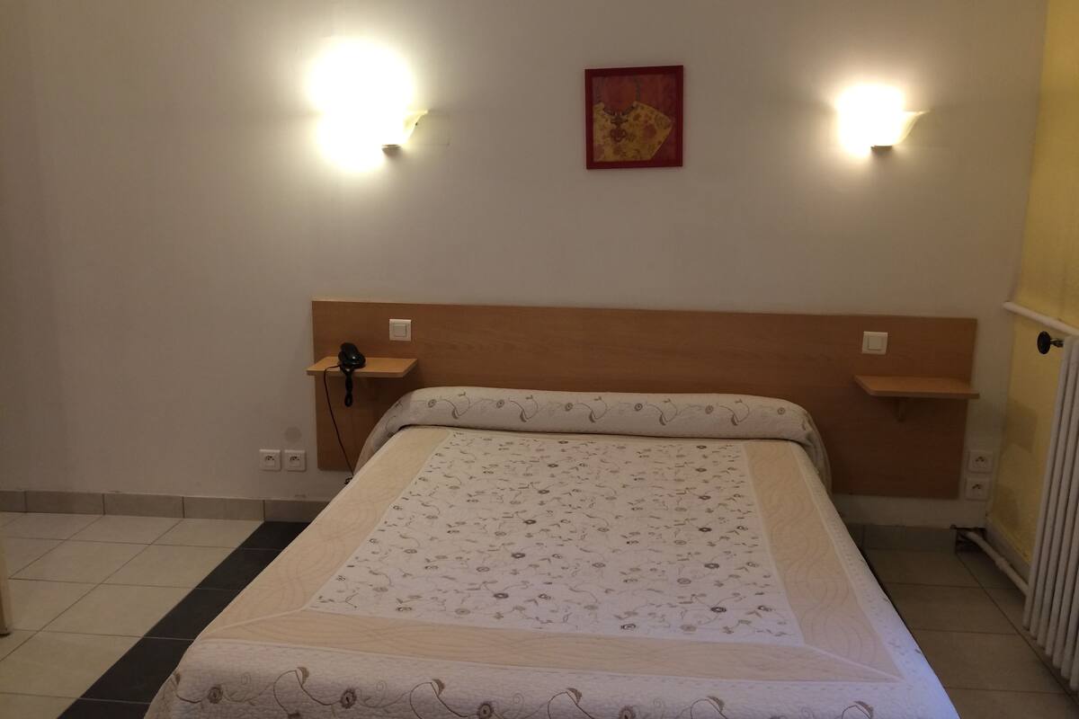 Un lit bien fait, avec une literie à motifs floraux, deux tables de chevet avec des lampes et un petit tableau accroché au mur.