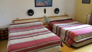 A double room with two beds, each with a striped bedspread, a wooden headboard, bedside tables, and wall-mounted lamps.