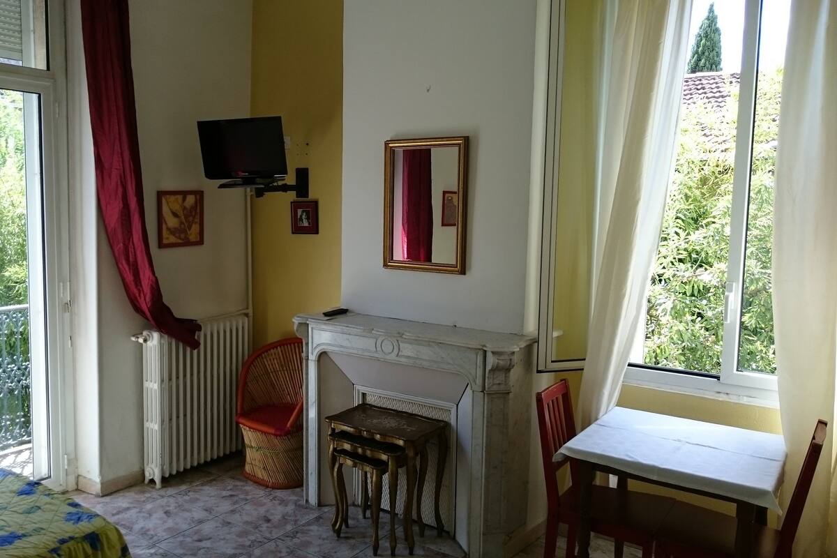 Une pièce avec une cheminée, un téléviseur fixé au mur, une fenêtre avec des rideaux et un balcon donnant sur un paysage verdoyant.