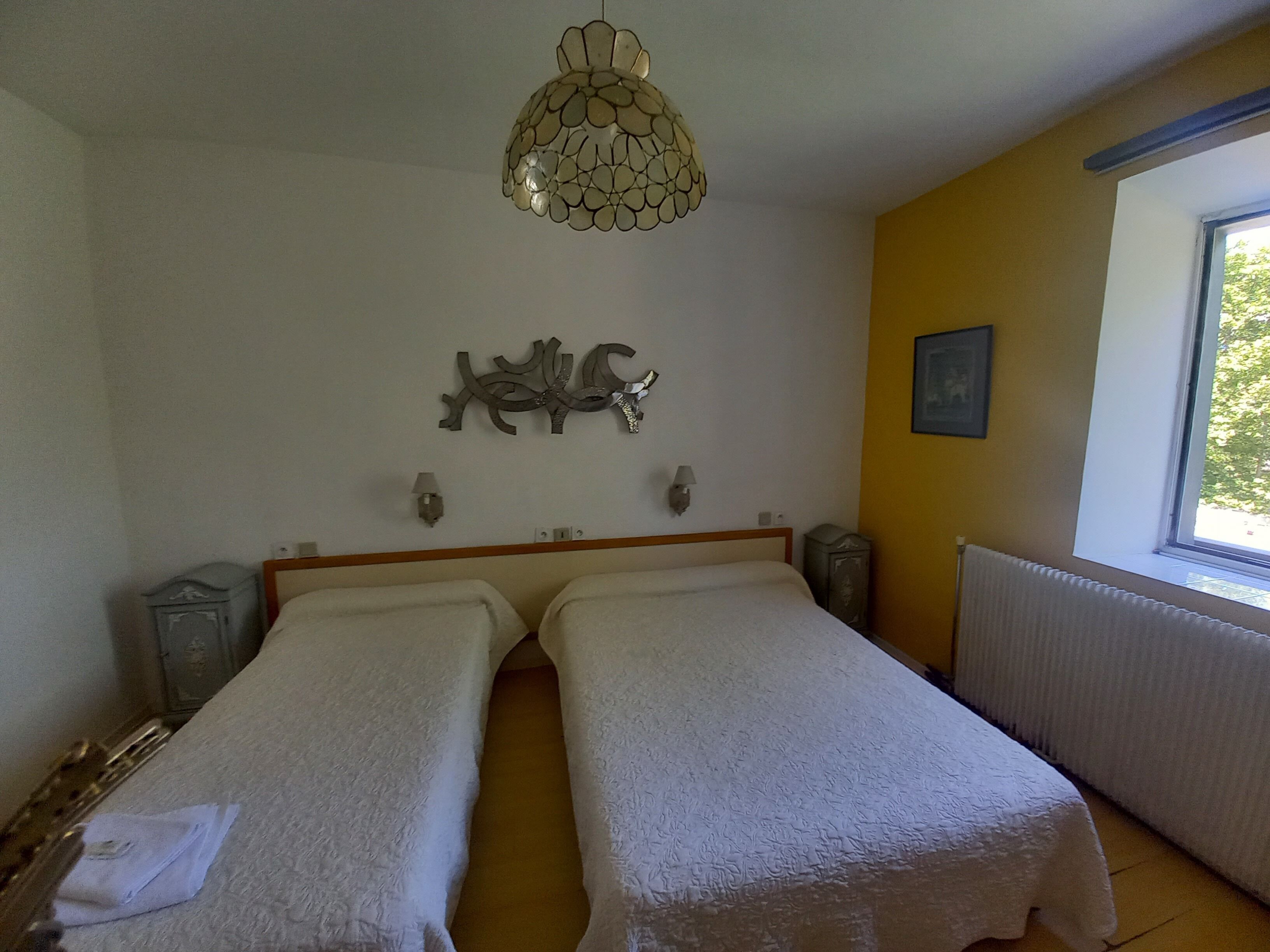 Una stanza con due letti, un elemento decorativo a parete, una finestra con vista e un termosifone.