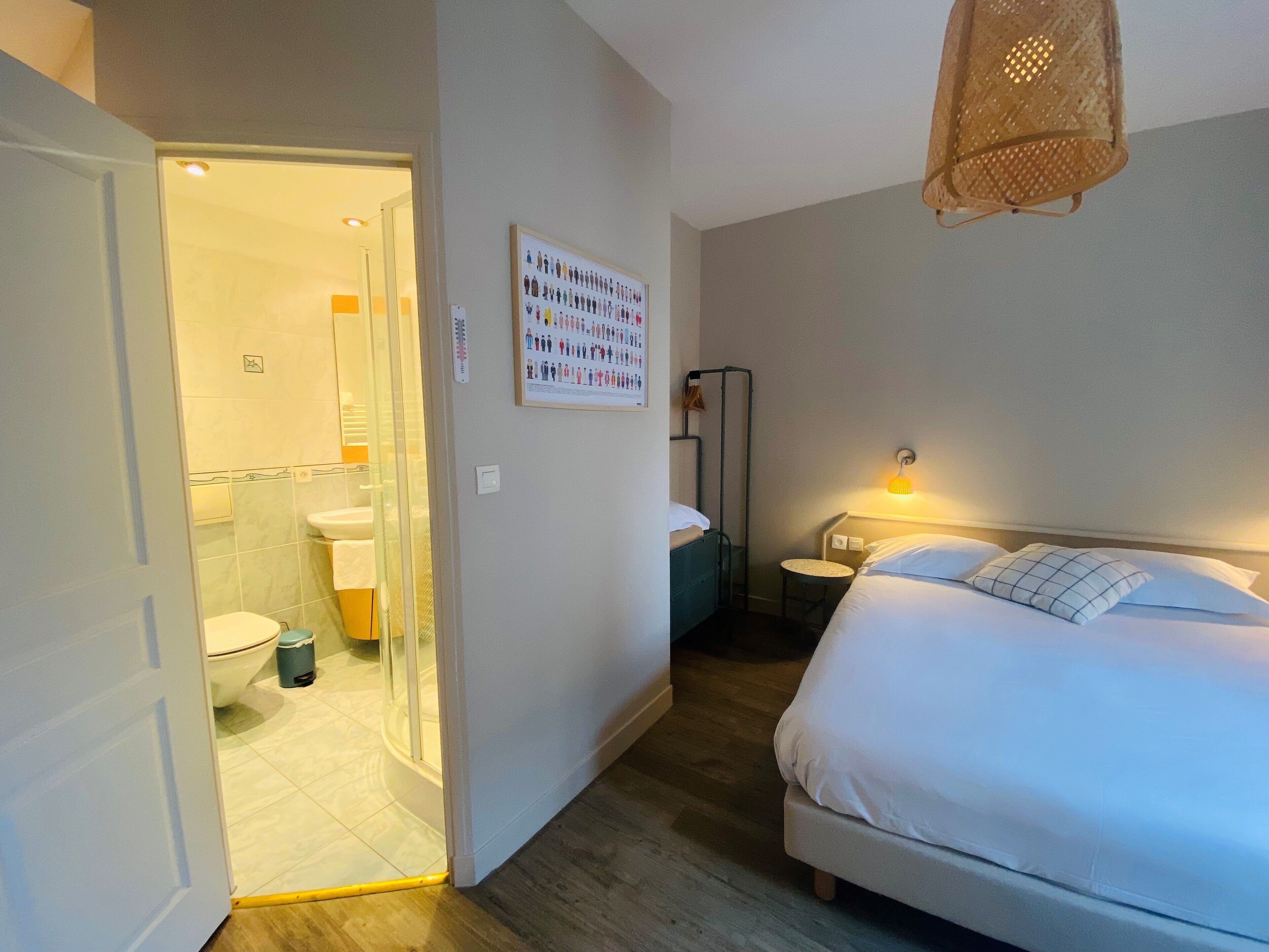 Una habitación de hotel con cama, mesita de noche, lámpara y un baño visible a través de una puerta abierta.