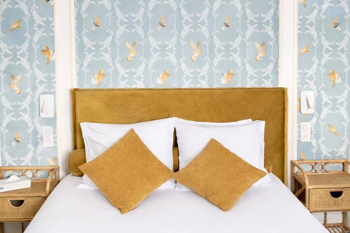 A bedroom with a bed, two pillows, a ceiling fan, and patterned wallpaper.