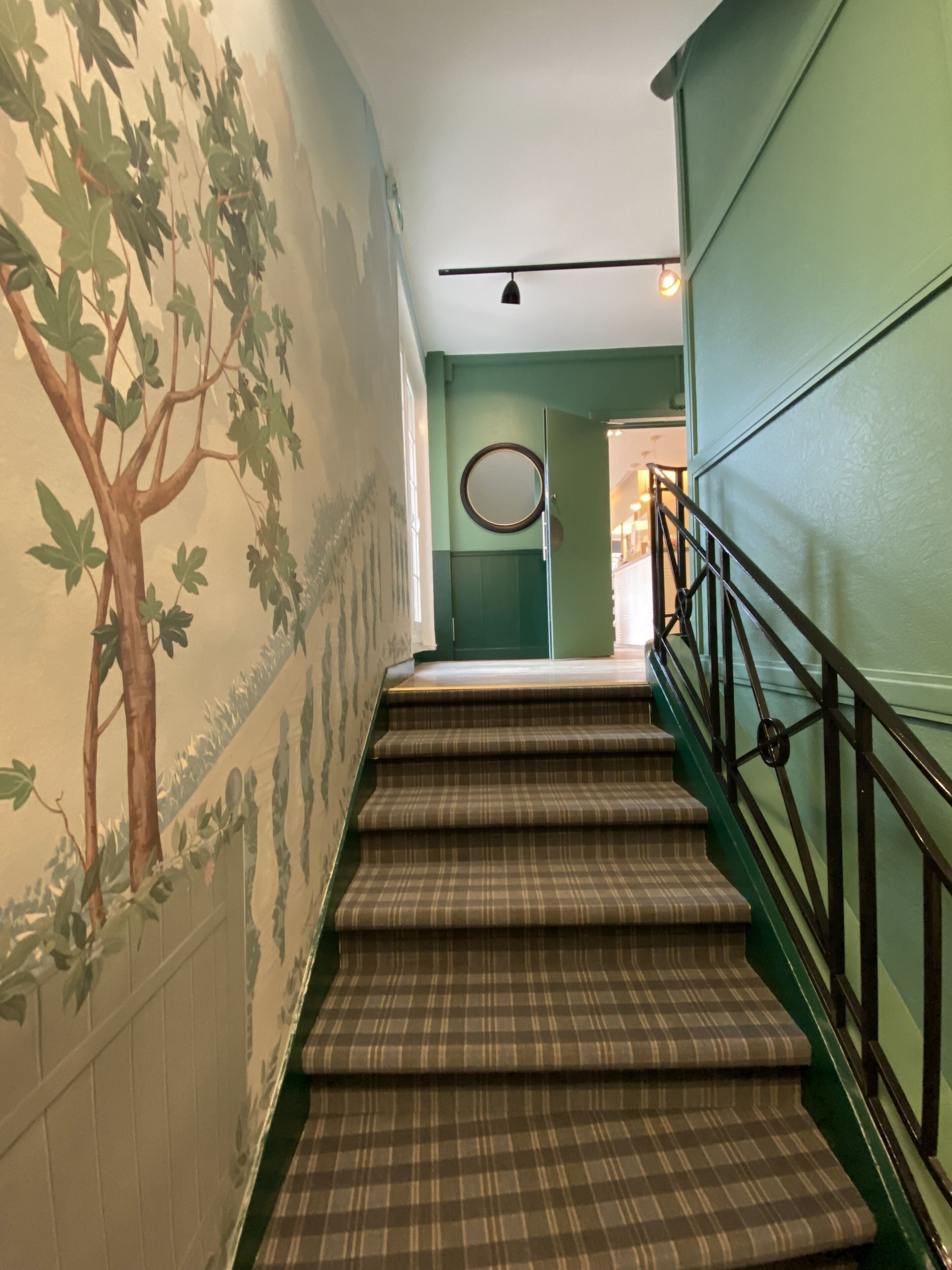 Una escalera con un suelo a cuadros y una pared verde con un mural de un árbol.