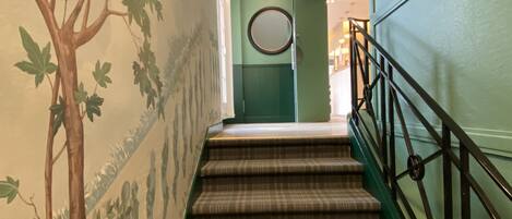 Una escalera con un suelo a cuadros y una pared verde con un mural de un árbol.