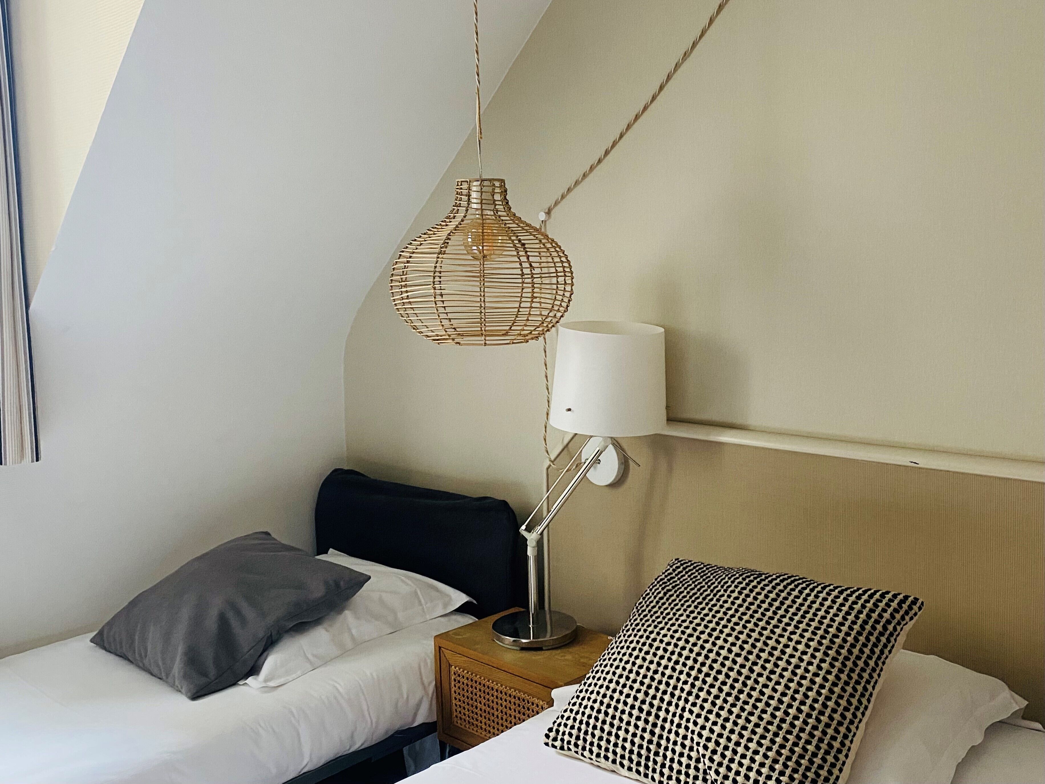 A small, cozy bedroom with a bed, a bedside table with a lamp, and a woven light fixture.