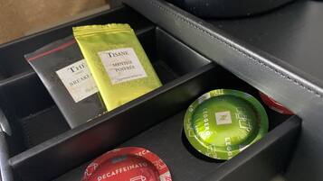 Un compartiment contenant divers articles, notamment un sachet vert portant la mention « TISANE MENTHE POIVRÉE », un sachet rouge portant la mention « DÉCAFÉINÉ » et un récipient noir sur lequel est inscrit « ESPRESSO ».