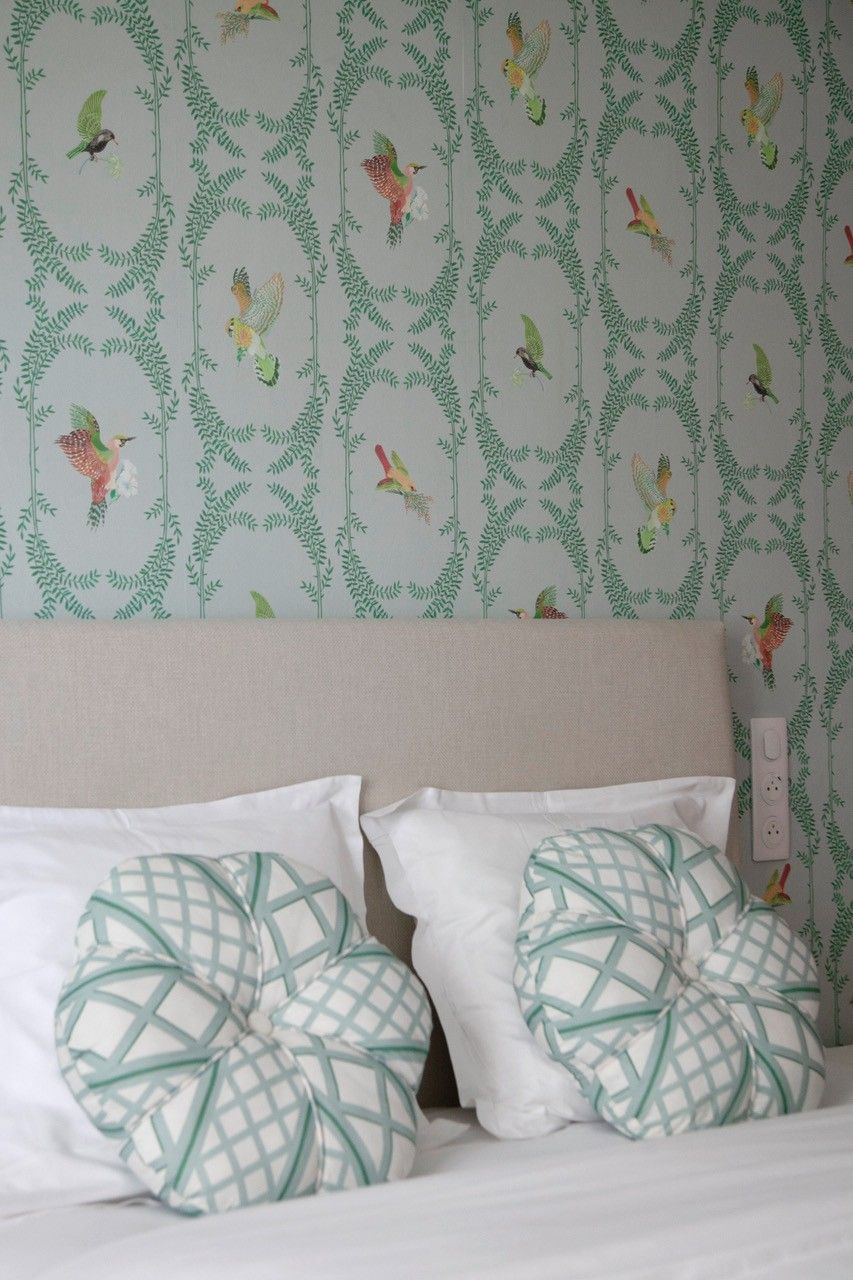 A bedroom with a bed, two pillows with a geometric pattern, and a wall with a wallpaper design featuring birds and foliage.