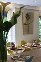 A dining area with a table set for breakfast, including pastries, a fruit bowl, and a painting of an owl on the wall.