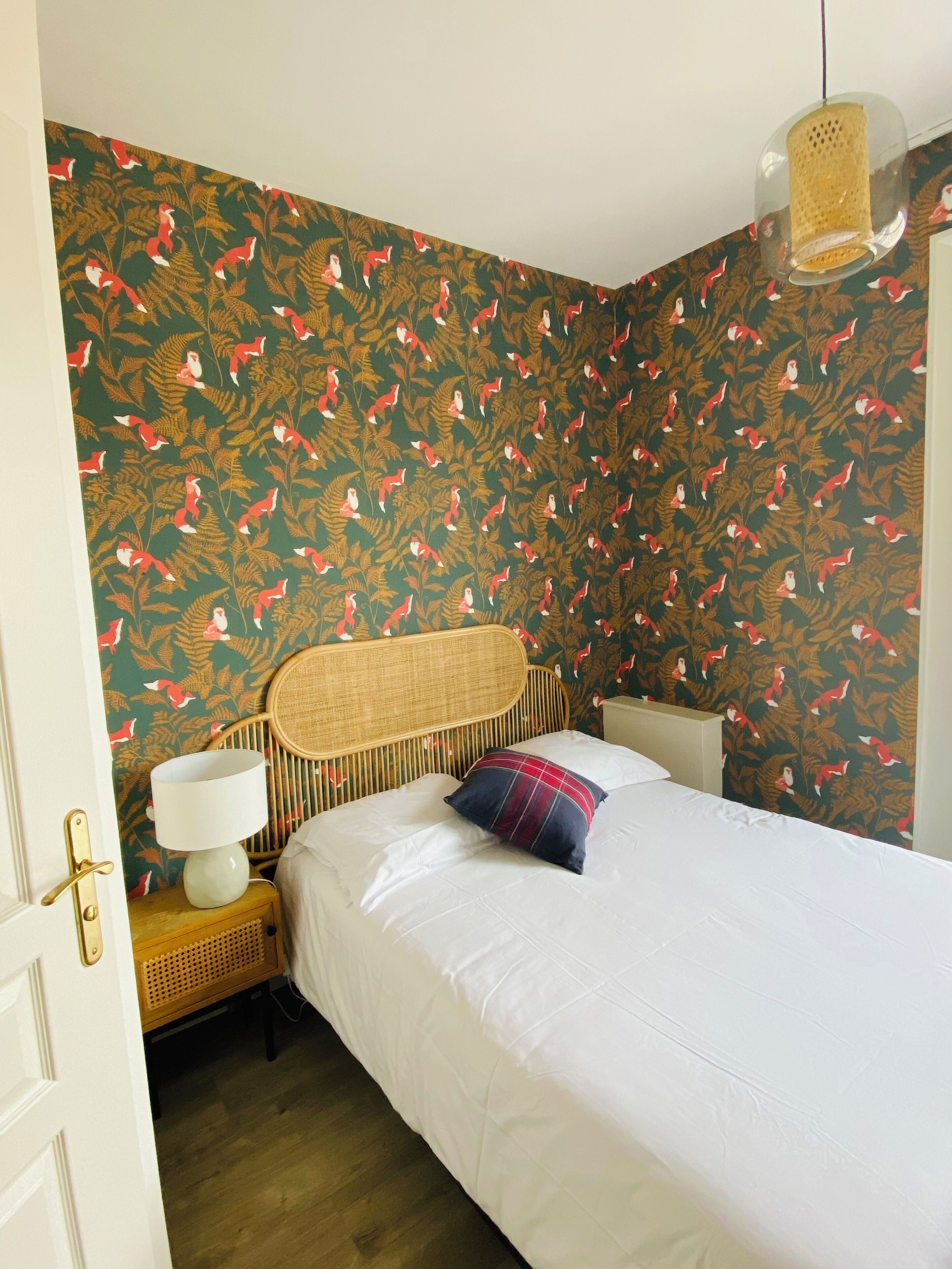 A bedroom with a bed, a nightstand, a lamp, and a wicker headboard.