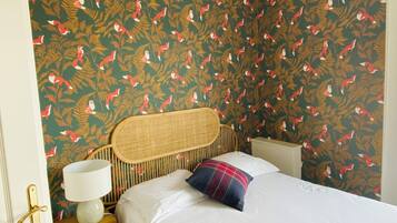 A bedroom with a bed, a nightstand, a lamp, and a wicker headboard.