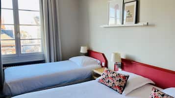 A hotel room with two single beds, a nightstand with a lamp, and a window with curtains.