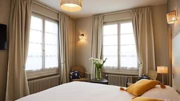 A hotel room with a large bed, two pillows, a small table with a vase of flowers, and a lamp.