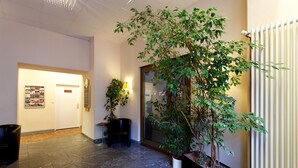 Un pasillo con una planta en maceta, una silla negra, una lámpara y un tablón de anuncios.