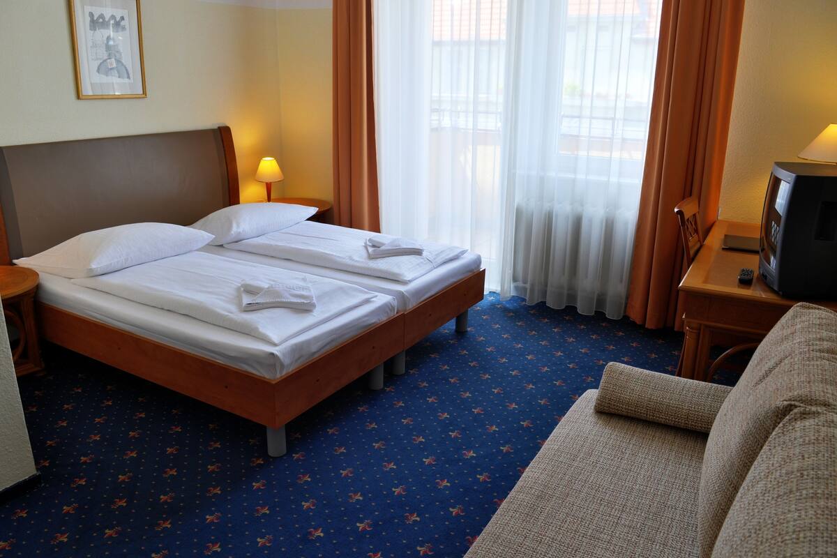 Habitación de hotel con dos camas individuales, televisión, una mesita y un sofá.