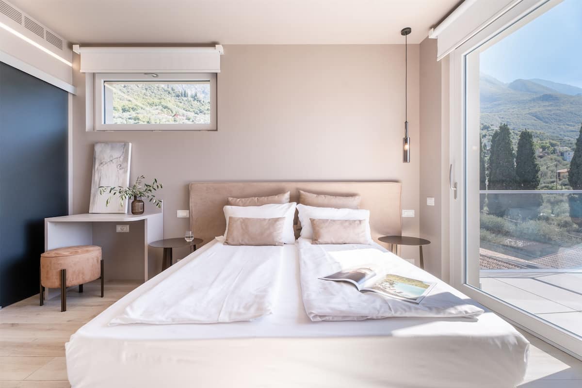 A modern bedroom with a large bed, a desk, and a view of the outdoors.