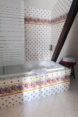 Une salle de bain avec une baignoire, des murs carrelés et une poutre en bois.