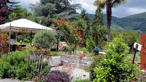 Ein Garten mit Laube, Steinmauer und verschiedenen Pflanzen.