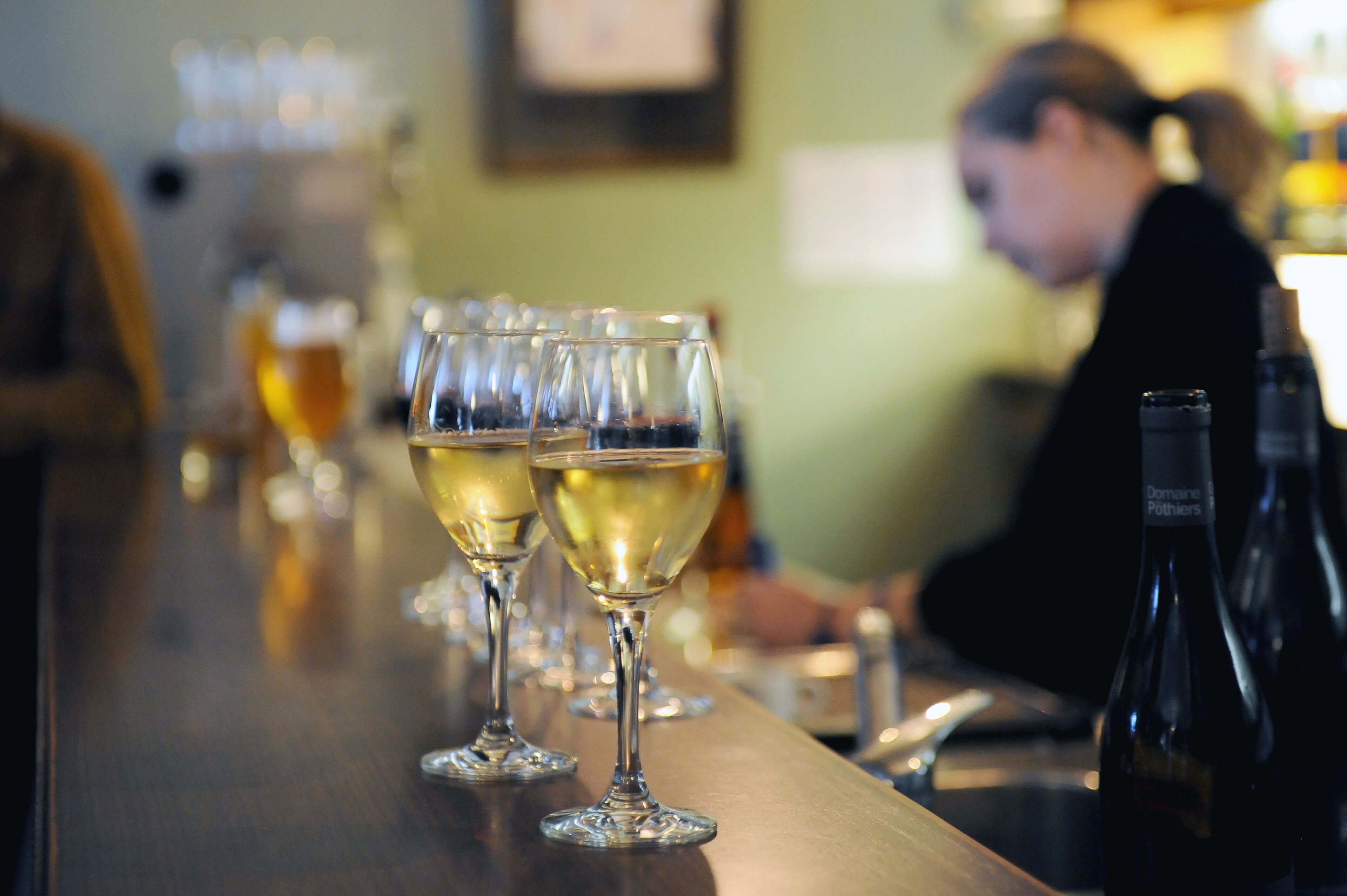 A bar with several glasses of white wine and a bottle of wine on the counter.