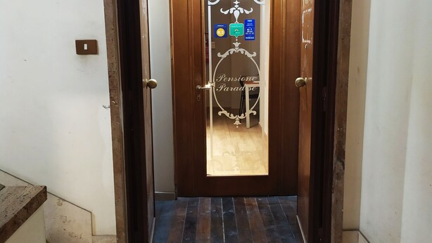 A hallway leading to a door with a frosted glass panel and a sign indicating amenities. - New Paradise (Rome)