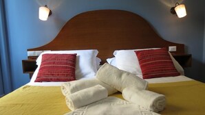 A neatly made bed with a wooden headboard, two wall-mounted lamps, and a yellow bedspread. - New Paradise (Rome)