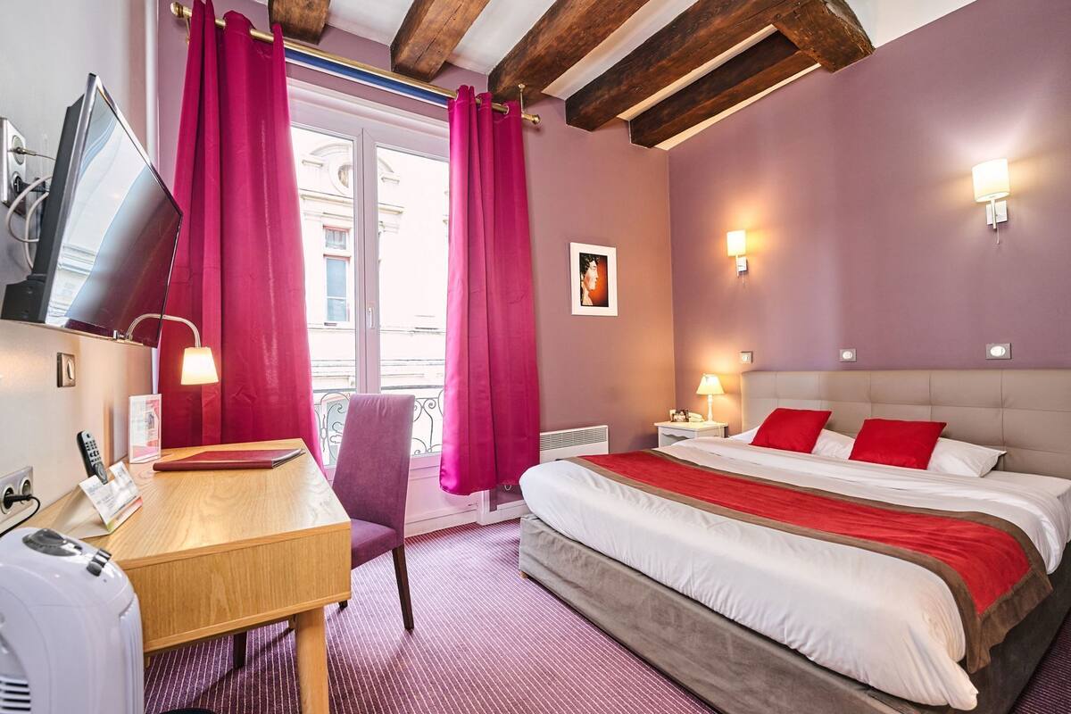 A hotel room with a bed, a desk, a chair, a TV, and a window with curtains.