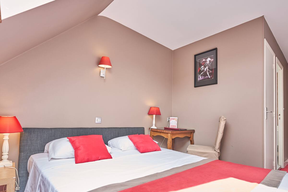 A bedroom with a bed, two bedside tables, a nightstand, a chair, a door, and a wall-mounted light fixture.