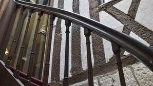 Una escalera de madera con barandilla de metal que conduce a una habitación con paredes de piedra y un ventanal grande.