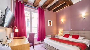 Habitación de hotel con cama, escritorio, silla, televisor y ventana con cortinas.