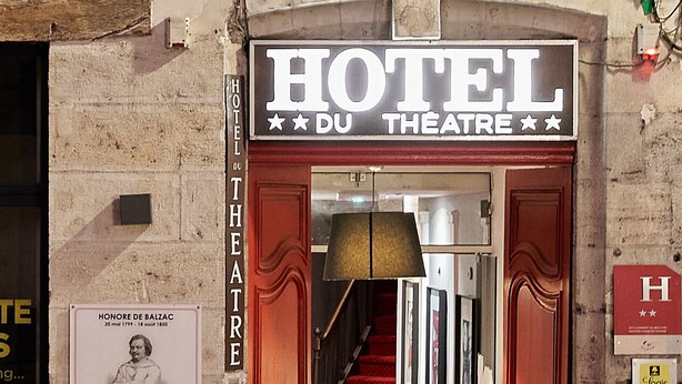 La entrada de un hotel con alfombra roja y un cartel que dice "HOTEL DU THEATRE".