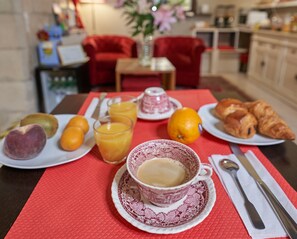 Une table de petit-déjeuner avec des assiettes de fruits, du jus d’orange, des croissants et une tasse de café.