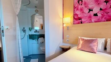 A hotel room with a shower, sink, toilet, and a bed with a large floral wall decoration.